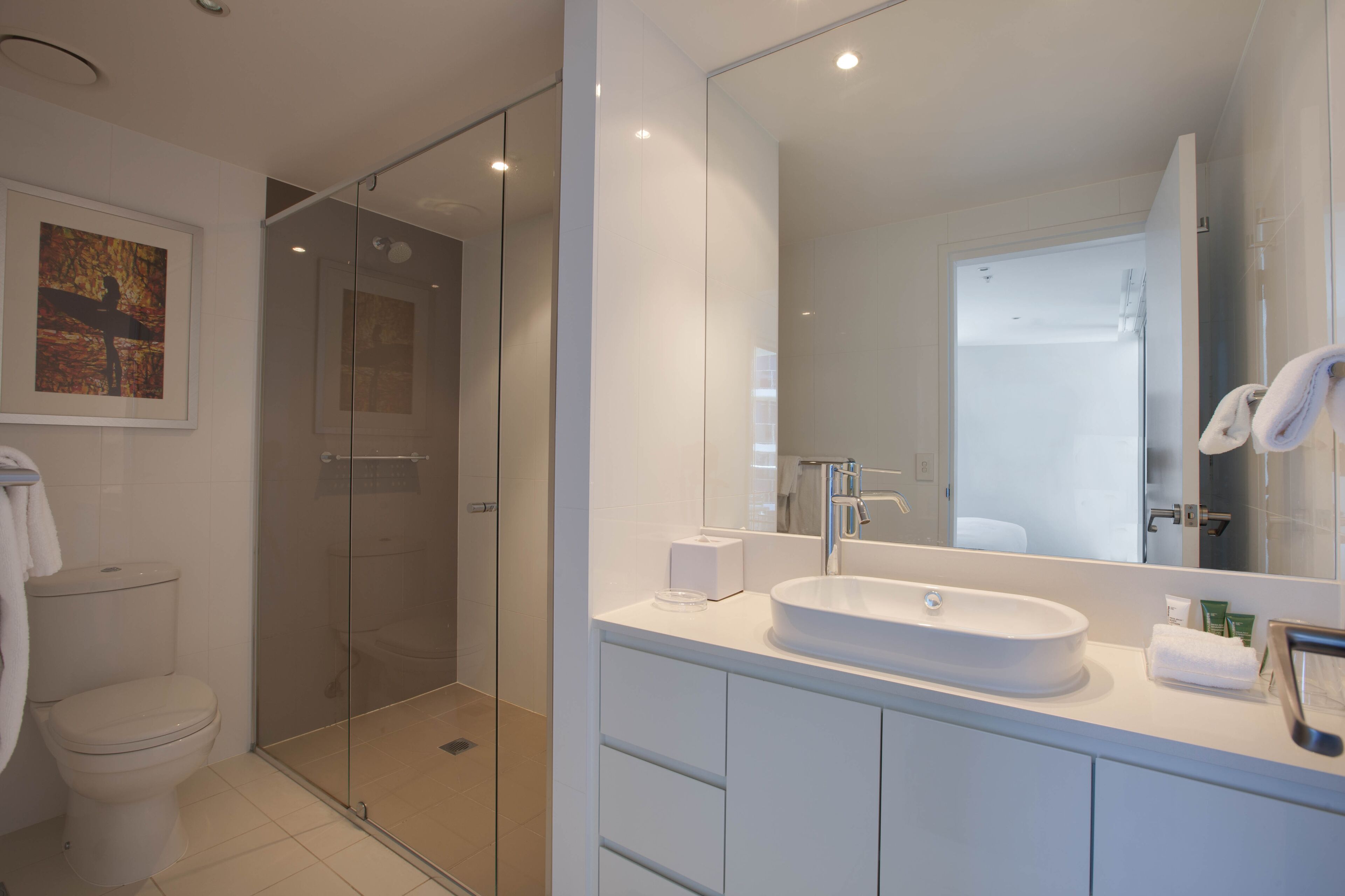 Een moderne badkamer met een douchecabine van glas, een grote spiegel en een witte wastafel.