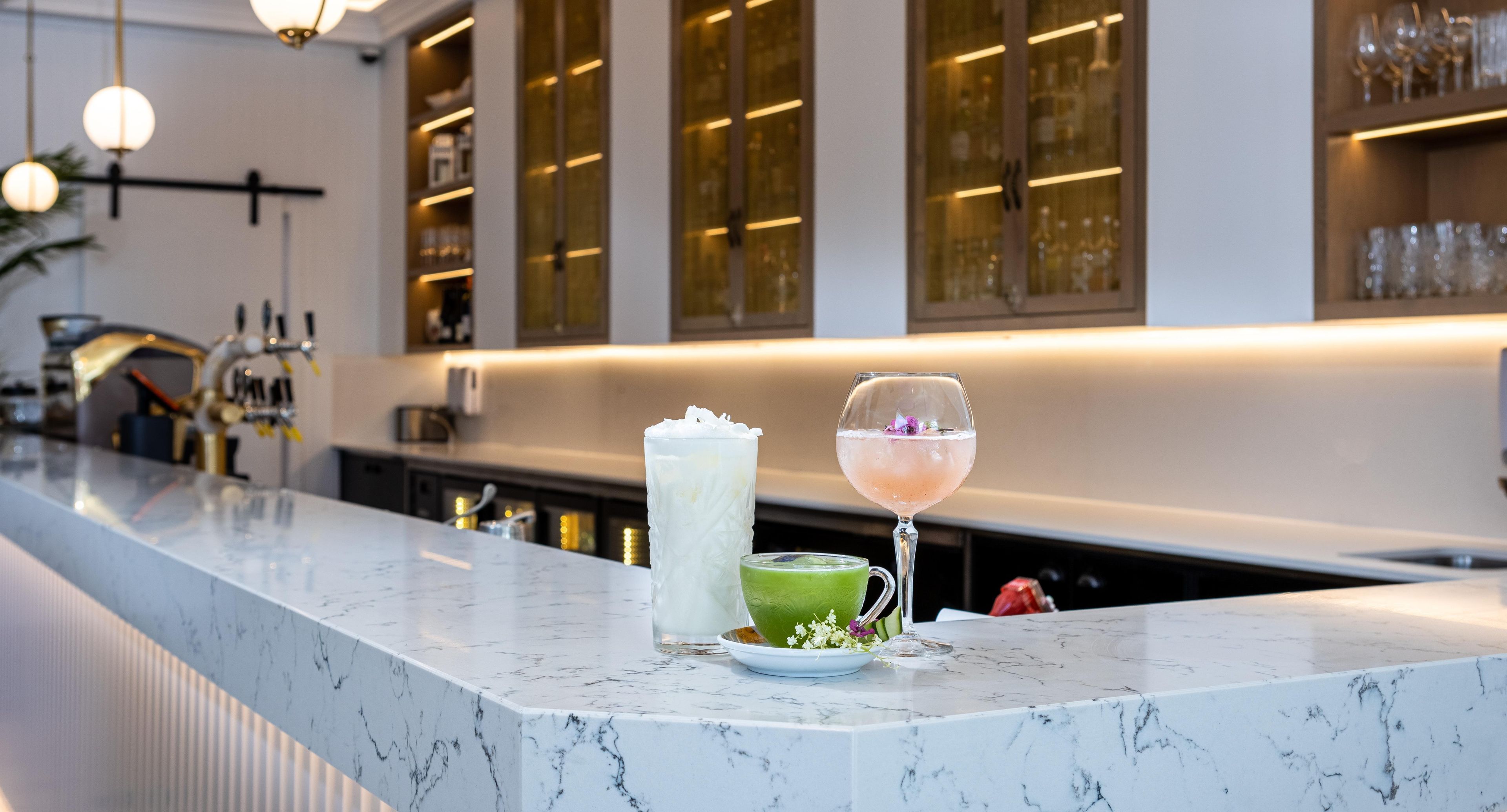 A bar area with a marble countertop, a glass of pink cocktail, and a green drink on a plate.