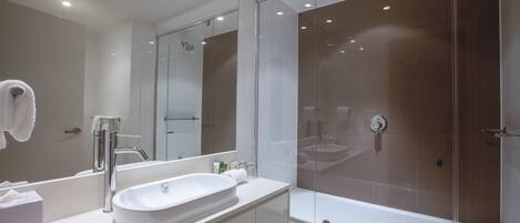 A modern bathroom with a large mirror, a white sink, and a glass-enclosed shower area.