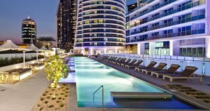 Una piscina en la azotea con sillas de descanso, rodeada de edificios modernos con balcones.