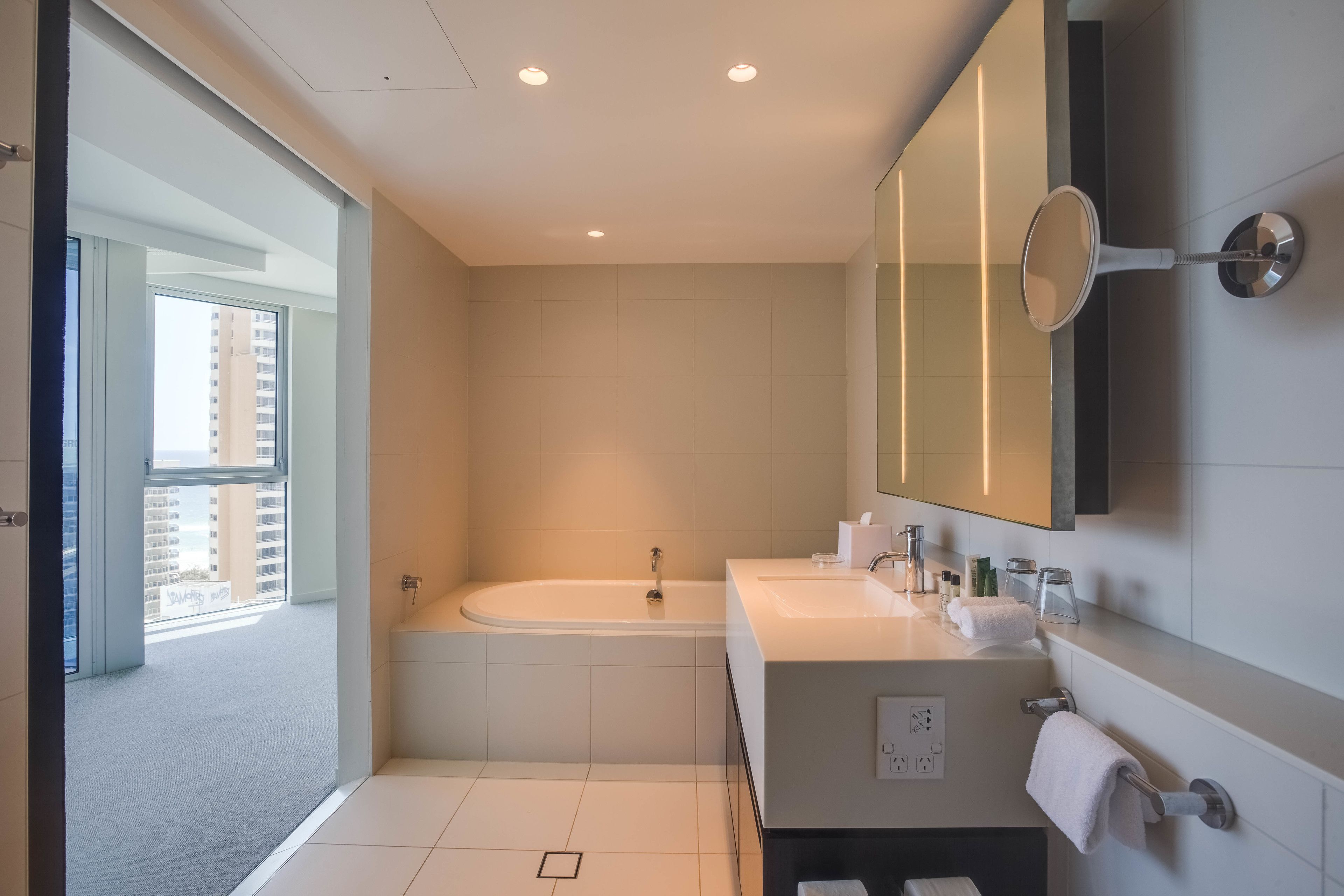 A modern bathroom with a bathtub, a large mirror, and a vanity with a sink.