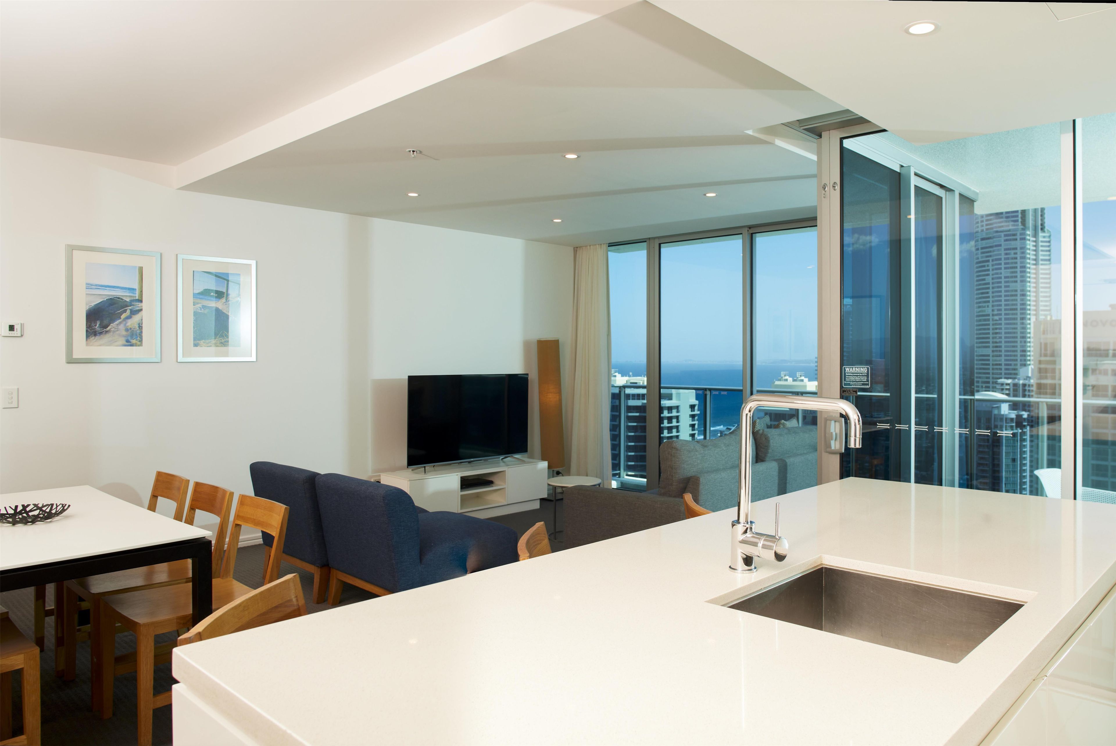 A modern kitchen with a built-in sink, dining area with chairs, and a television.