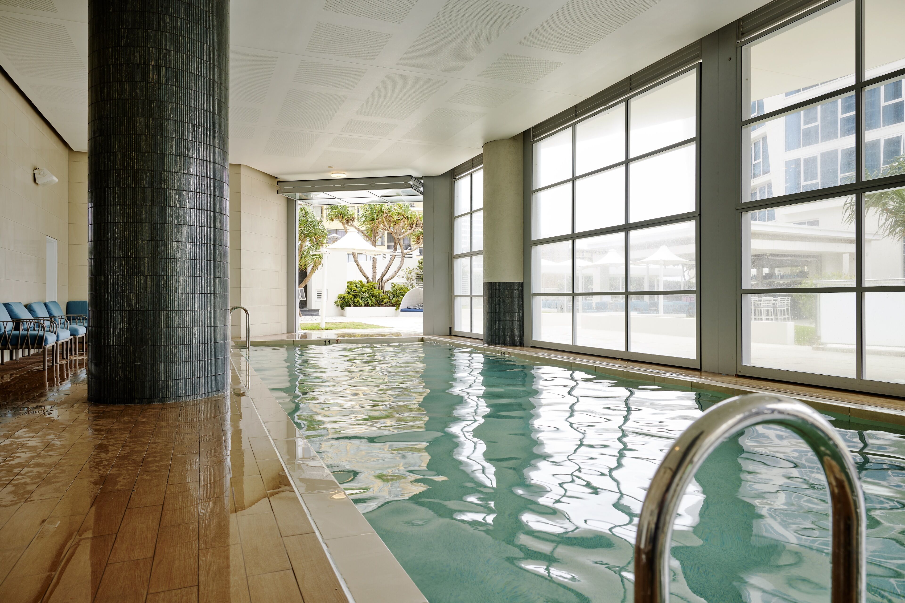 An indoor swimming pool with clear glass walls, a tiled floor, and a metal pool ladder.
