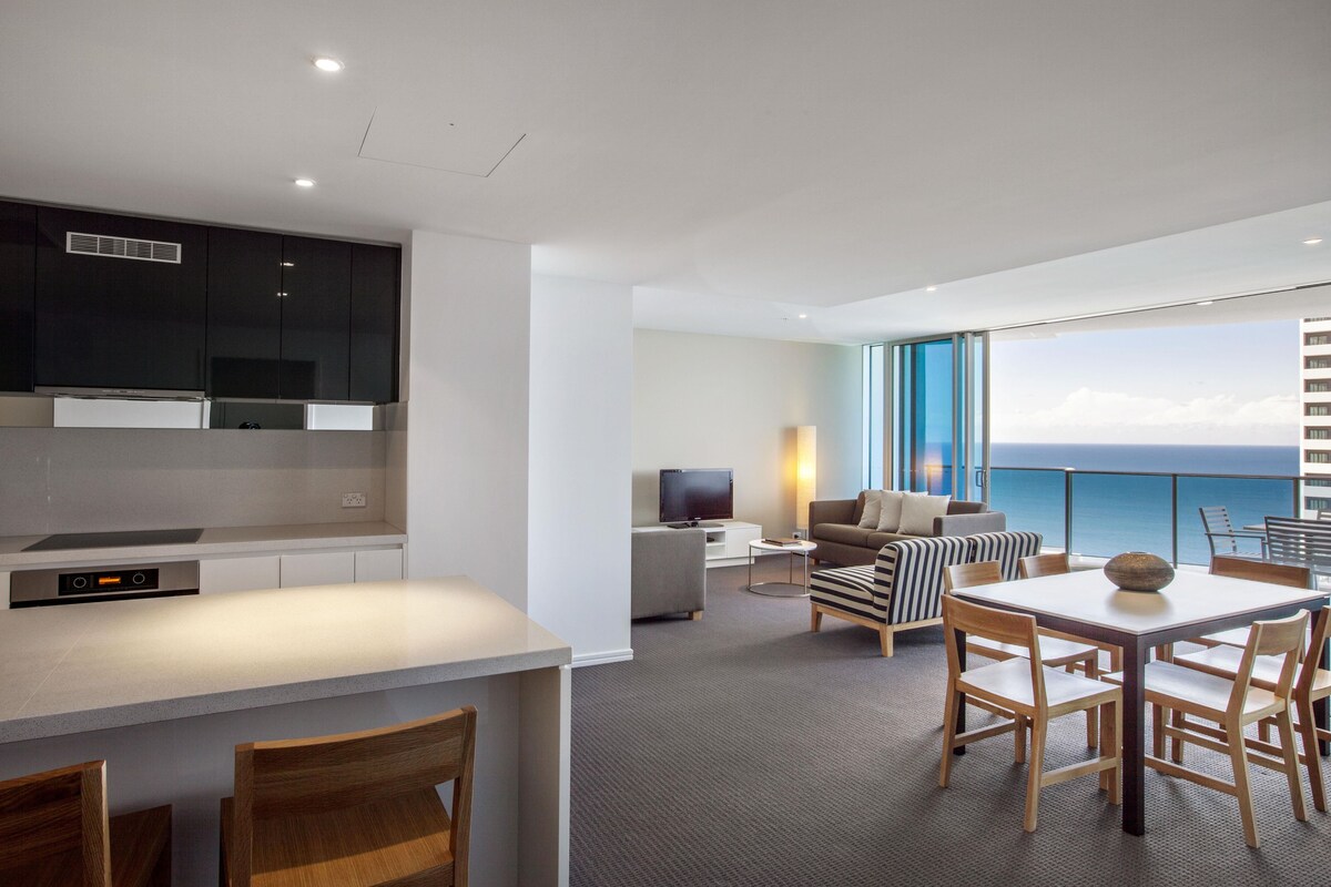 A modern hotel room with a kitchen, dining area, and a balcony with a view.