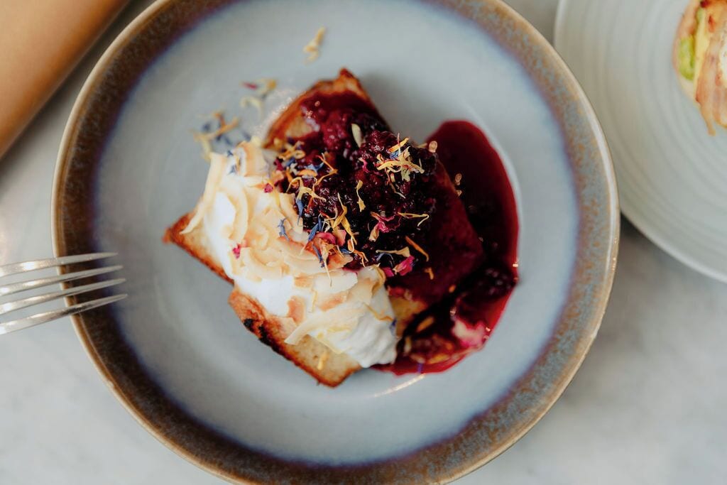 Un postre en un plato con crema batida y frutos rojos.