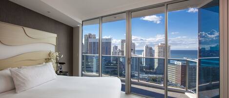 Ein modernes Hotelzimmer mit einem großen Bett, Blick auf die Stadt und einem Balkon mit Glastür.