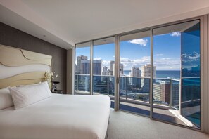 Una habitación de hotel moderna con una cama grande, vistas a la ciudad y un balcón con puerta de cristal.