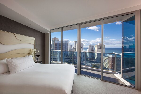 A modern hotel room with a large bed, a view of the cityscape, and a balcony with a glass door.