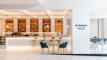 A modern bar area with a counter, bar stools, and shelves stocked with bottles and glasses.