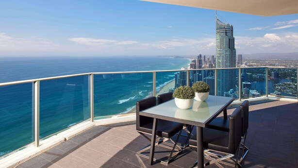 Een balkon met een tafel en stoelen, met uitzicht op een stadsbeeld en de oceaan.