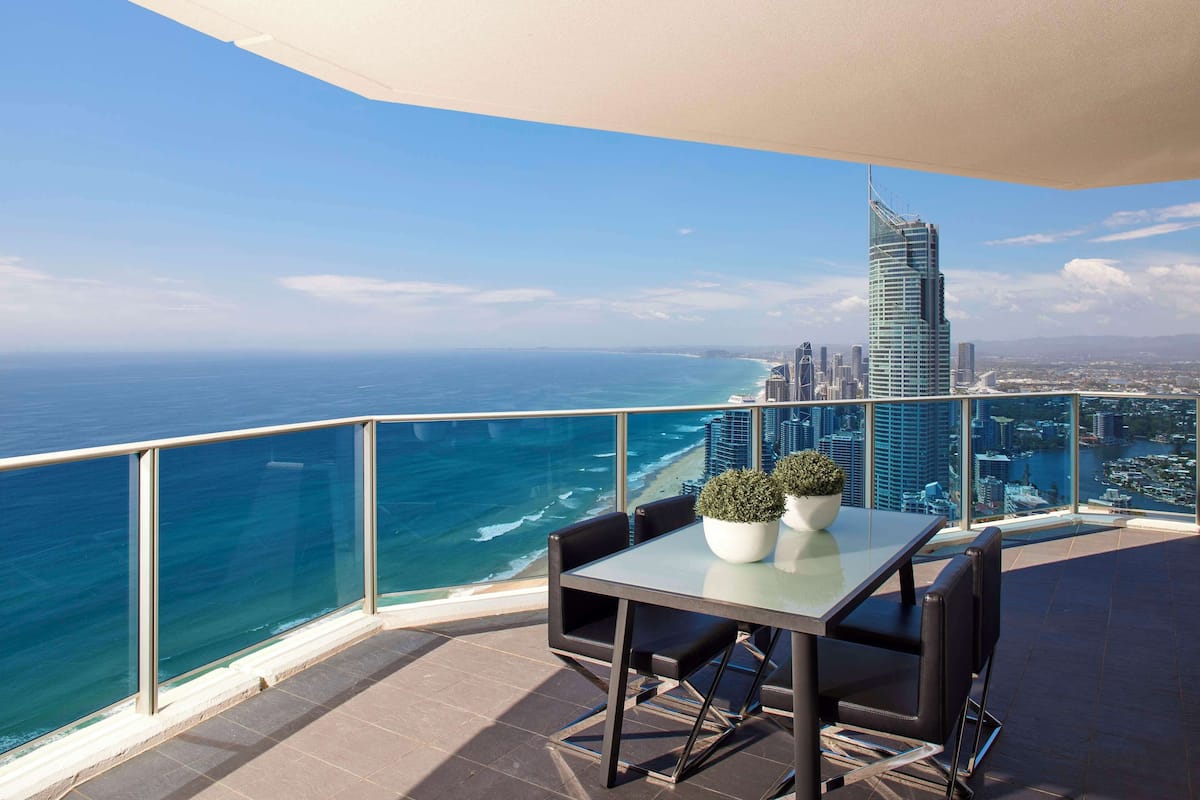 A balcony with a table and chairs, overlooking a city skyline and the ocean.