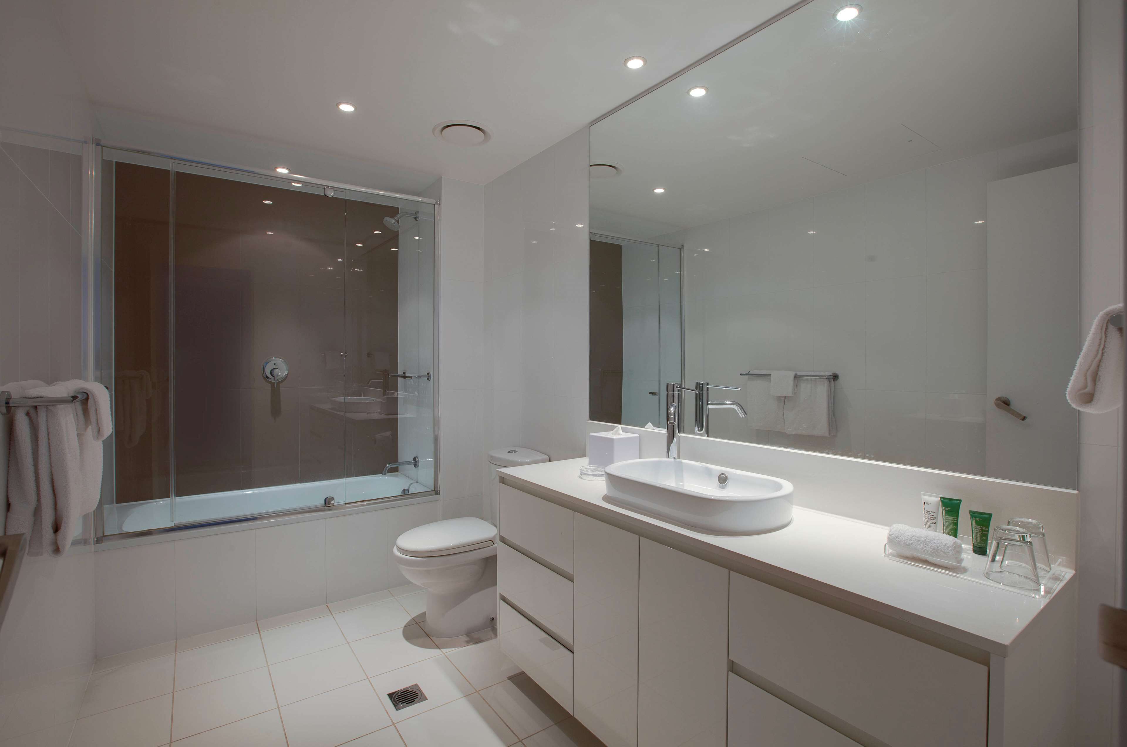 Une salle de bain moderne avec une douche à parois de verre, un lavabo blanc et un grand miroir.