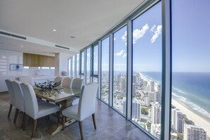 Un comedor moderno con una mesa y sillas de vidrio, amplias ventanas con vista a la ciudad y al océano.