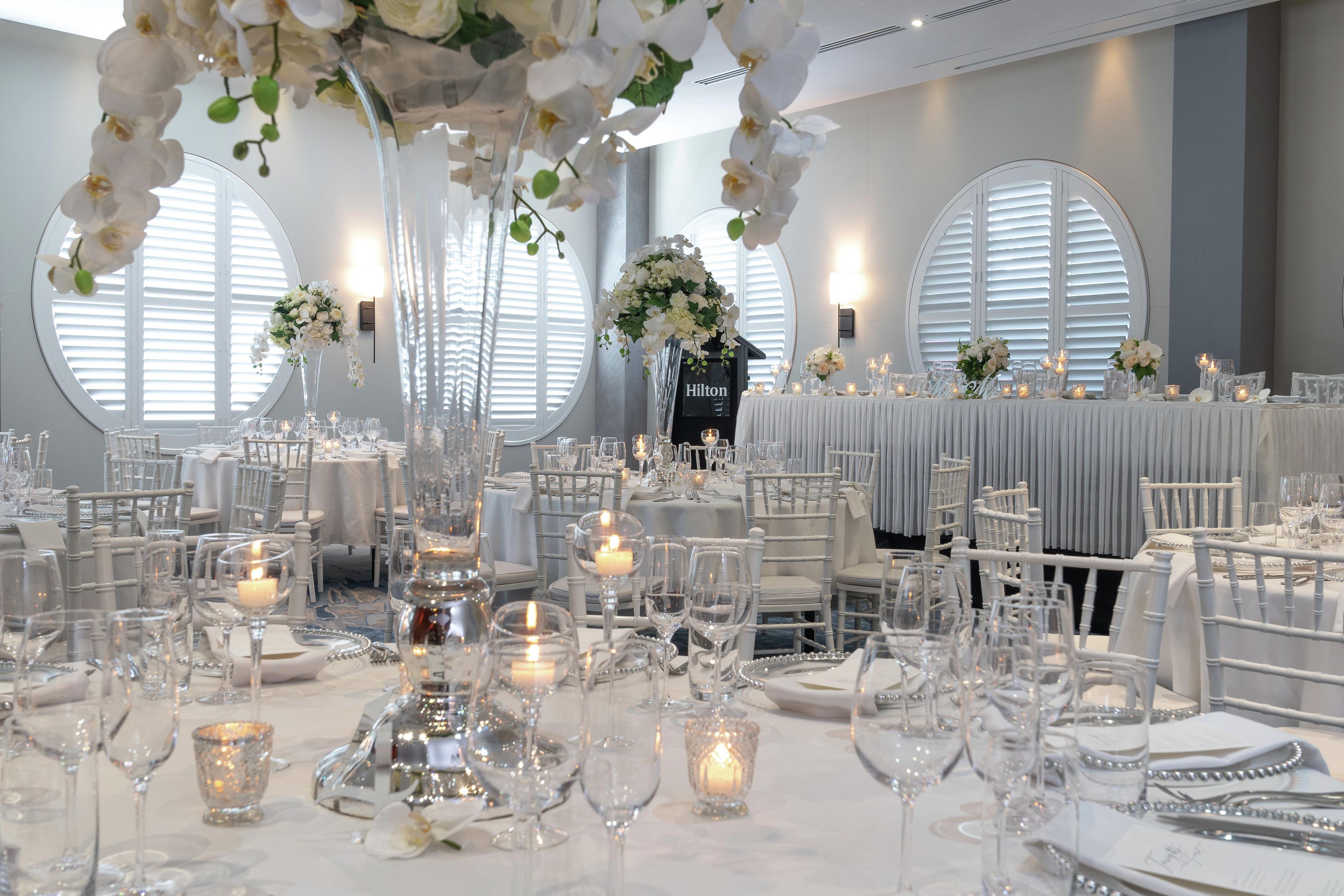 A formal dining area with round tables, white chairs, and floral centerpieces.