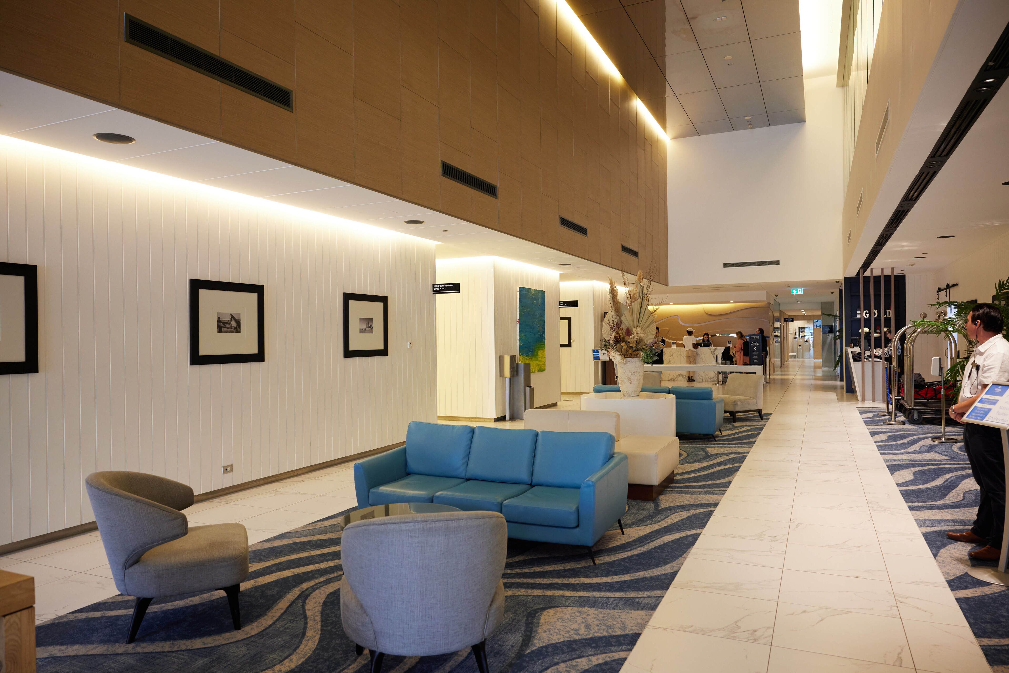 Eine Hotellobby mit einem blauen Sofa, Sesseln, einem Empfangsbereich und gerahmten Bildern an den Wänden.