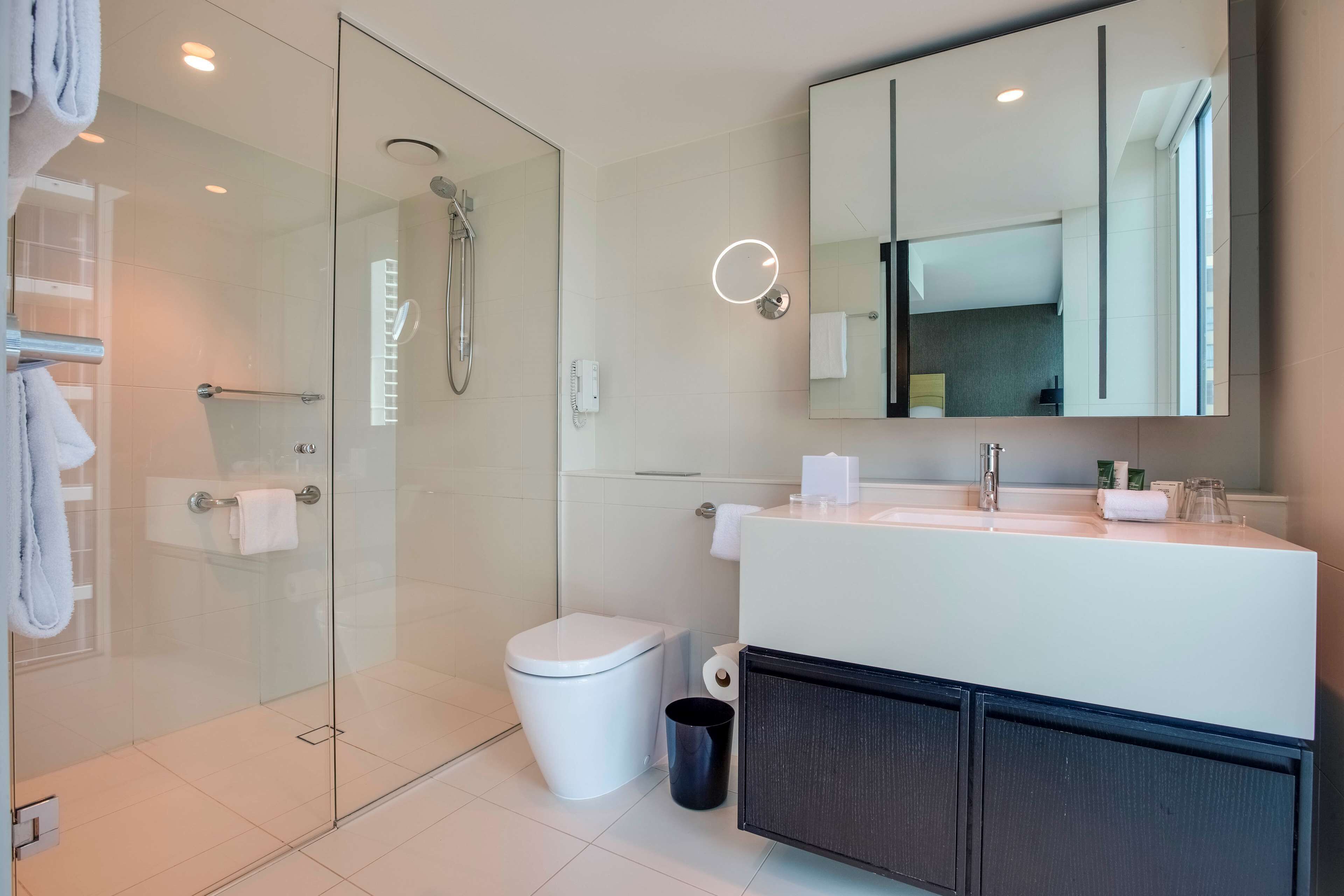 Une salle de bain moderne avec une douche à parois de verre, des toilettes blanches et un meuble-lavabo avec un miroir.