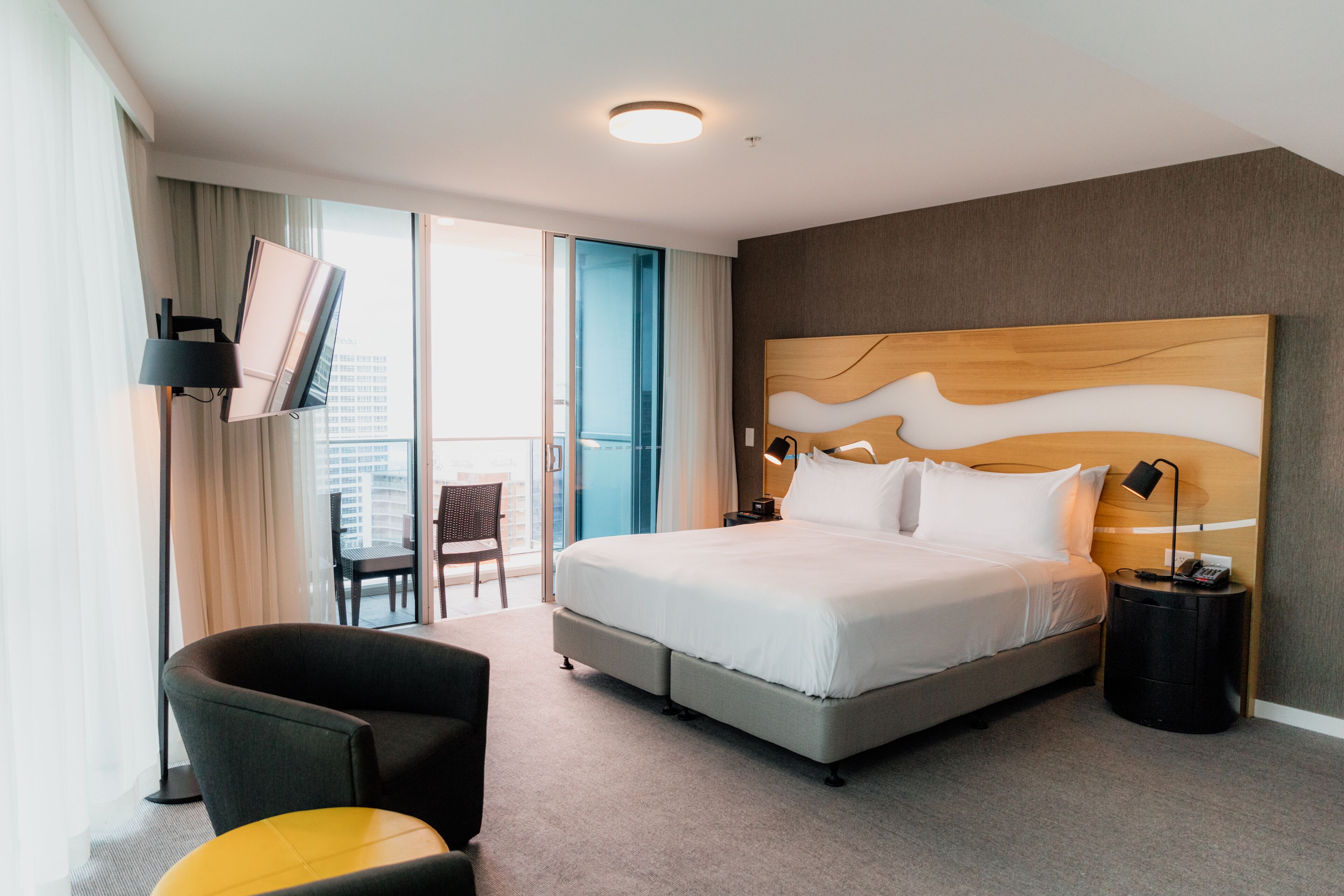 Habitación de hotel moderna con una cama grande, un escritorio, una silla y vistas de la ciudad a través de las puertas del balcón.