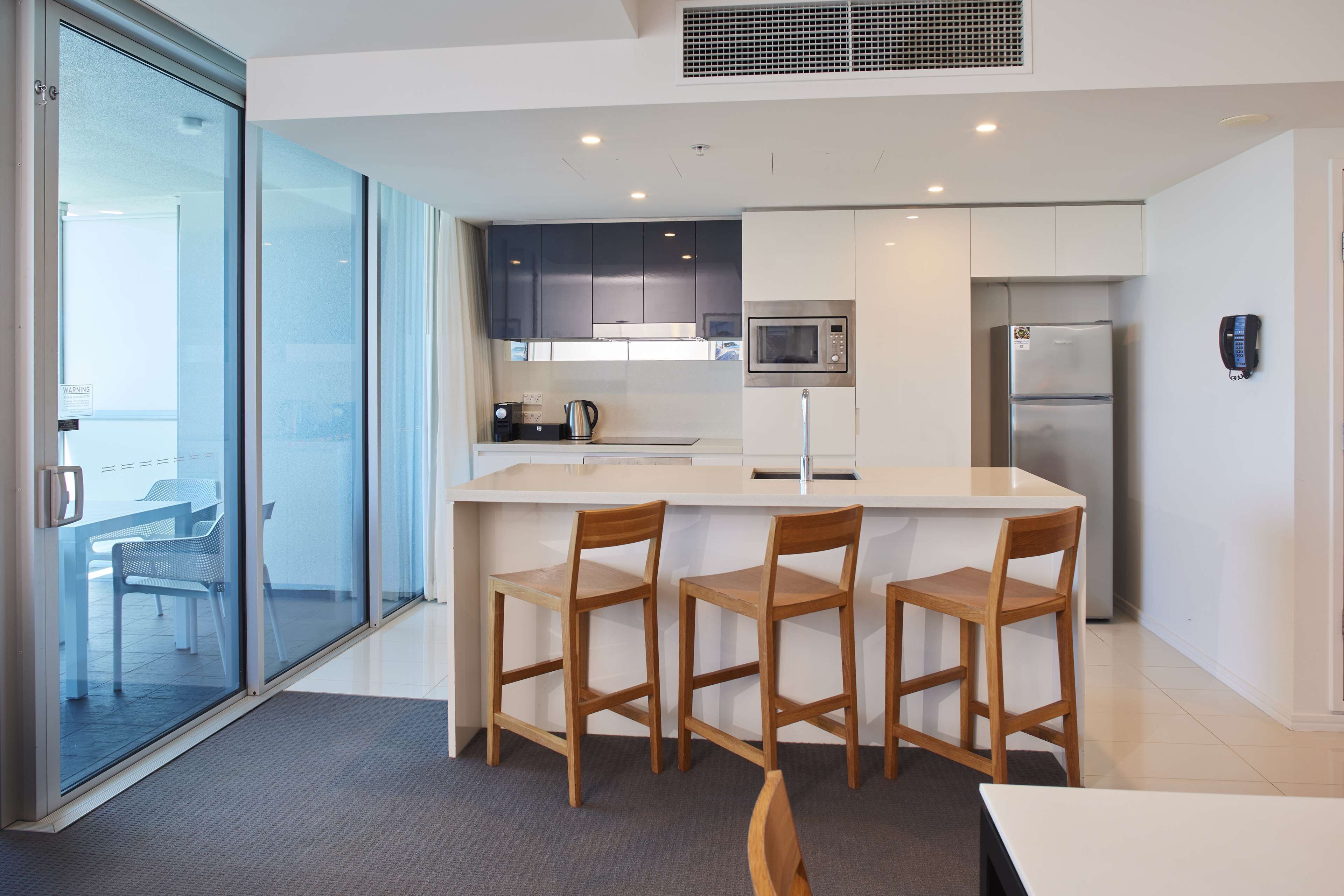 Een moderne keuken met een centraal eiland, houten stoelen, een magnetron en een koelkast.