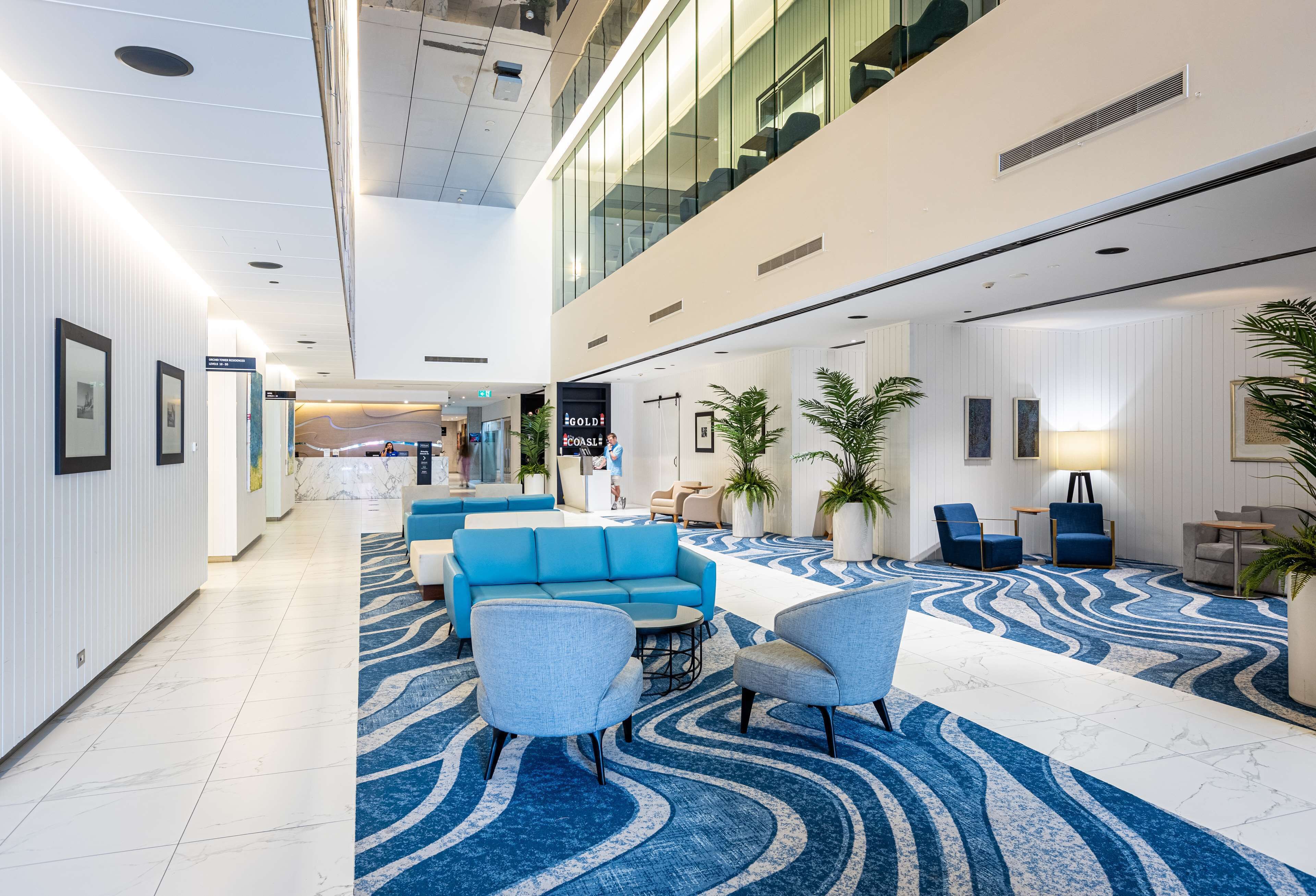 Een moderne lobby met een blauw-wit betegeld tapijt, zithoeken en een receptiebalie.