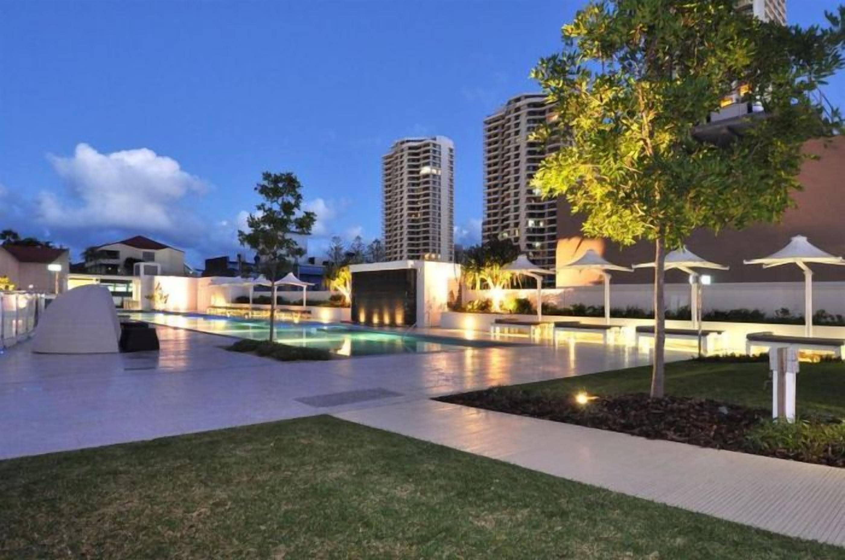 A modern hotel courtyard with a swimming pool, lounge areas, and a view of surrounding high-rise buildings.