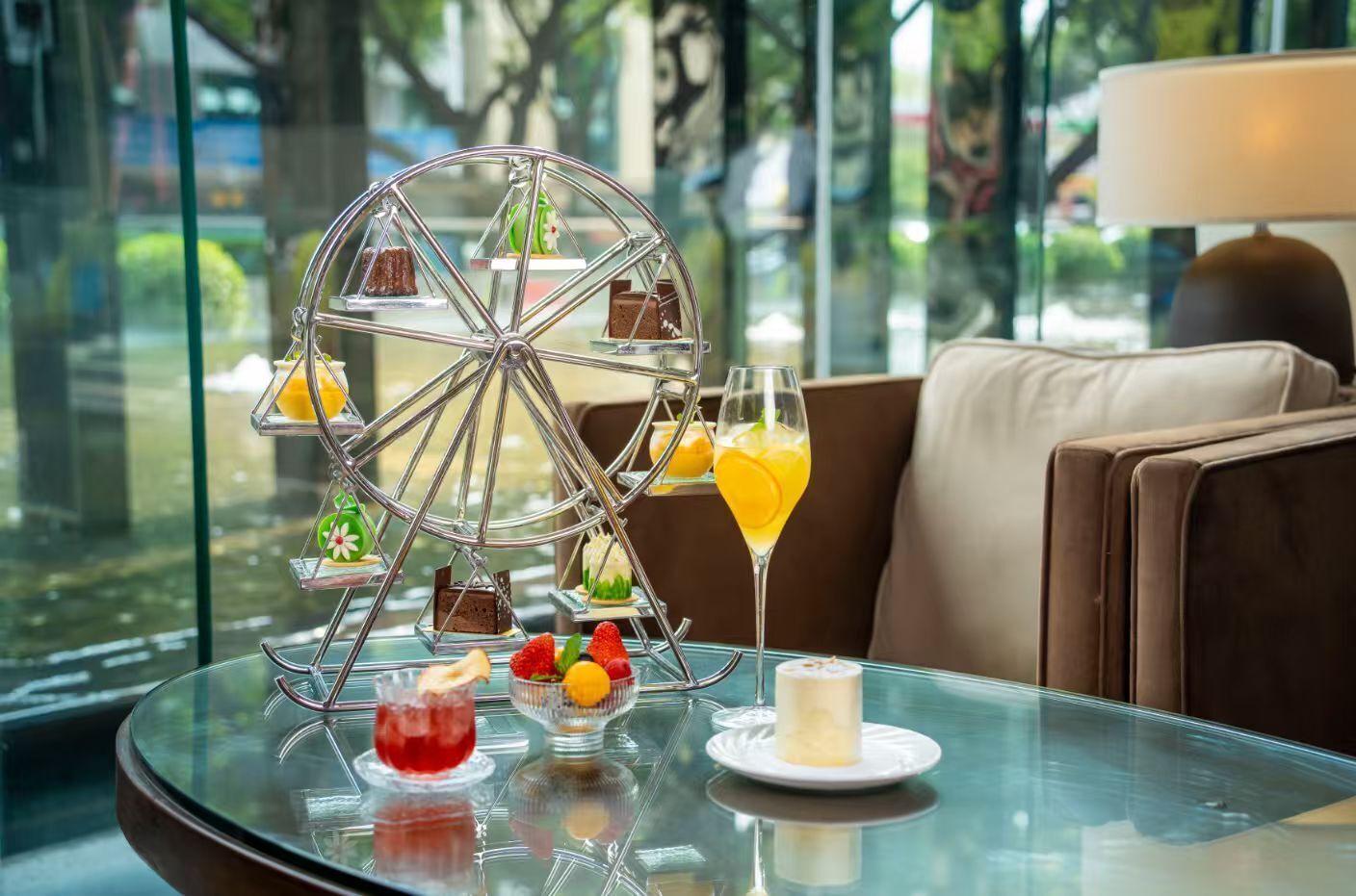 Una mesa de cristal con un carrito de postres, un vaso de zumo de naranja y una vela.