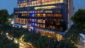 Un hotel moderno de varios pisos con fachada de vidrio, ventanas iluminadas y un llamativo letrero de "Hilton".