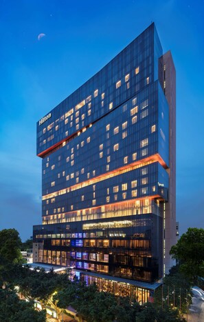 Un hotel moderno de varios pisos con fachada de vidrio, ventanas iluminadas y un llamativo letrero de "Hilton".