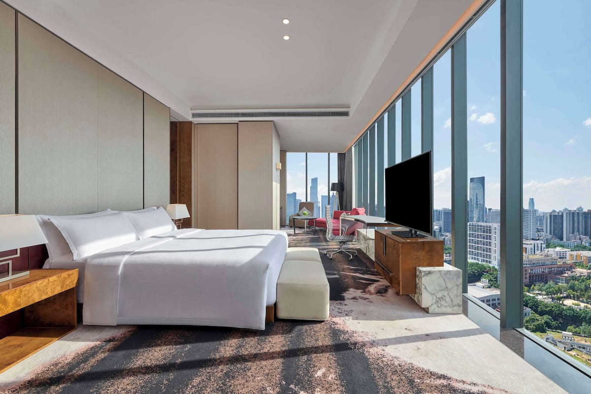A modern hotel room with a large bed, a desk, a TV, and a city view.
