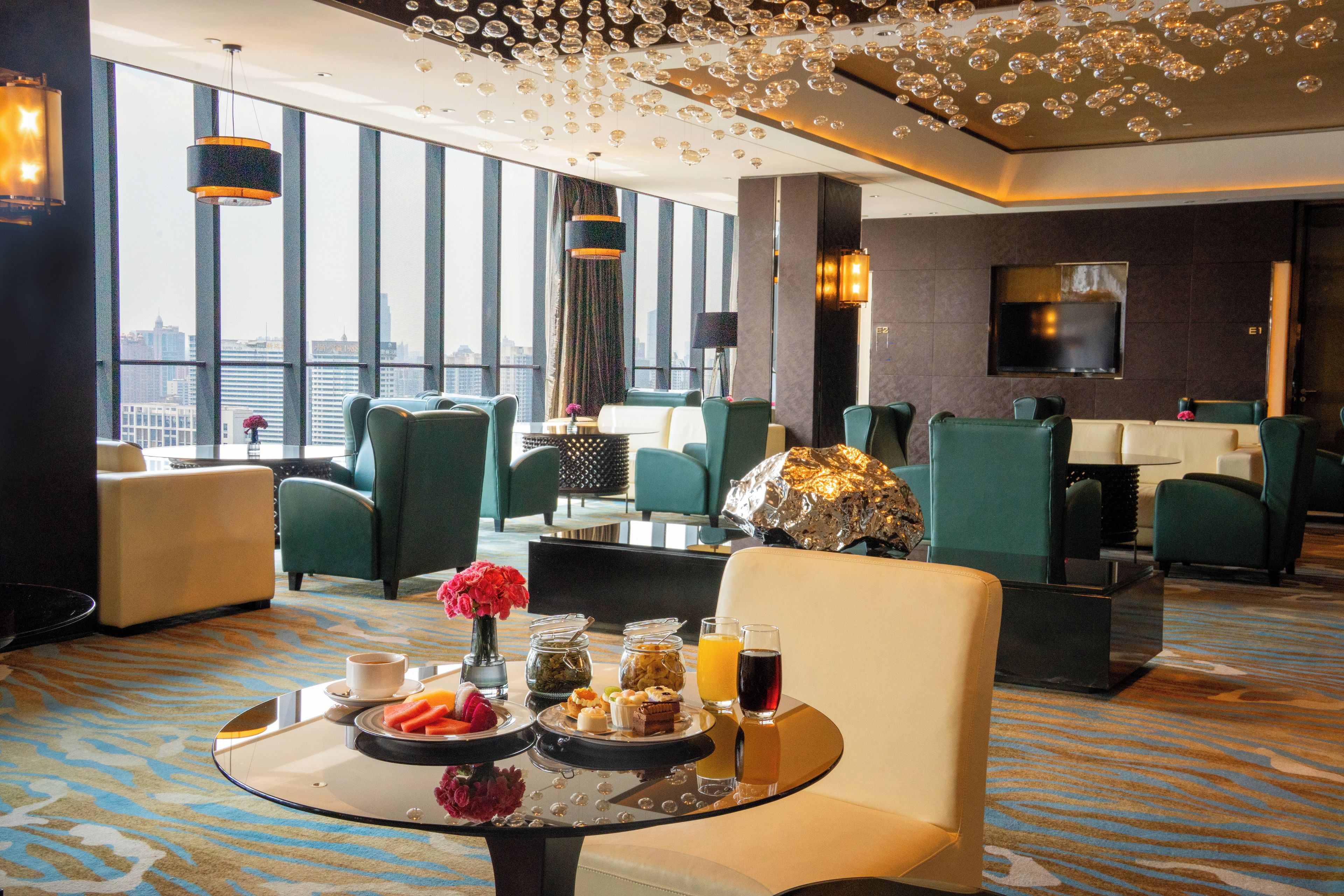 A hotel lobby with seating, a coffee table with snacks, and a city view.