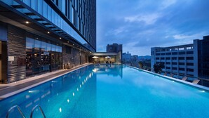 Un hotel moderno con piscina infinita en la azotea, ventanas amplias y vistas panorámicas de la ciudad.