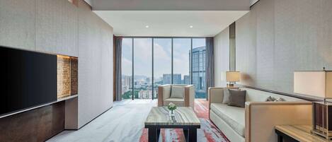 A modern hotel room with a large TV, a sofa, a coffee table, and a view of the city skyline.