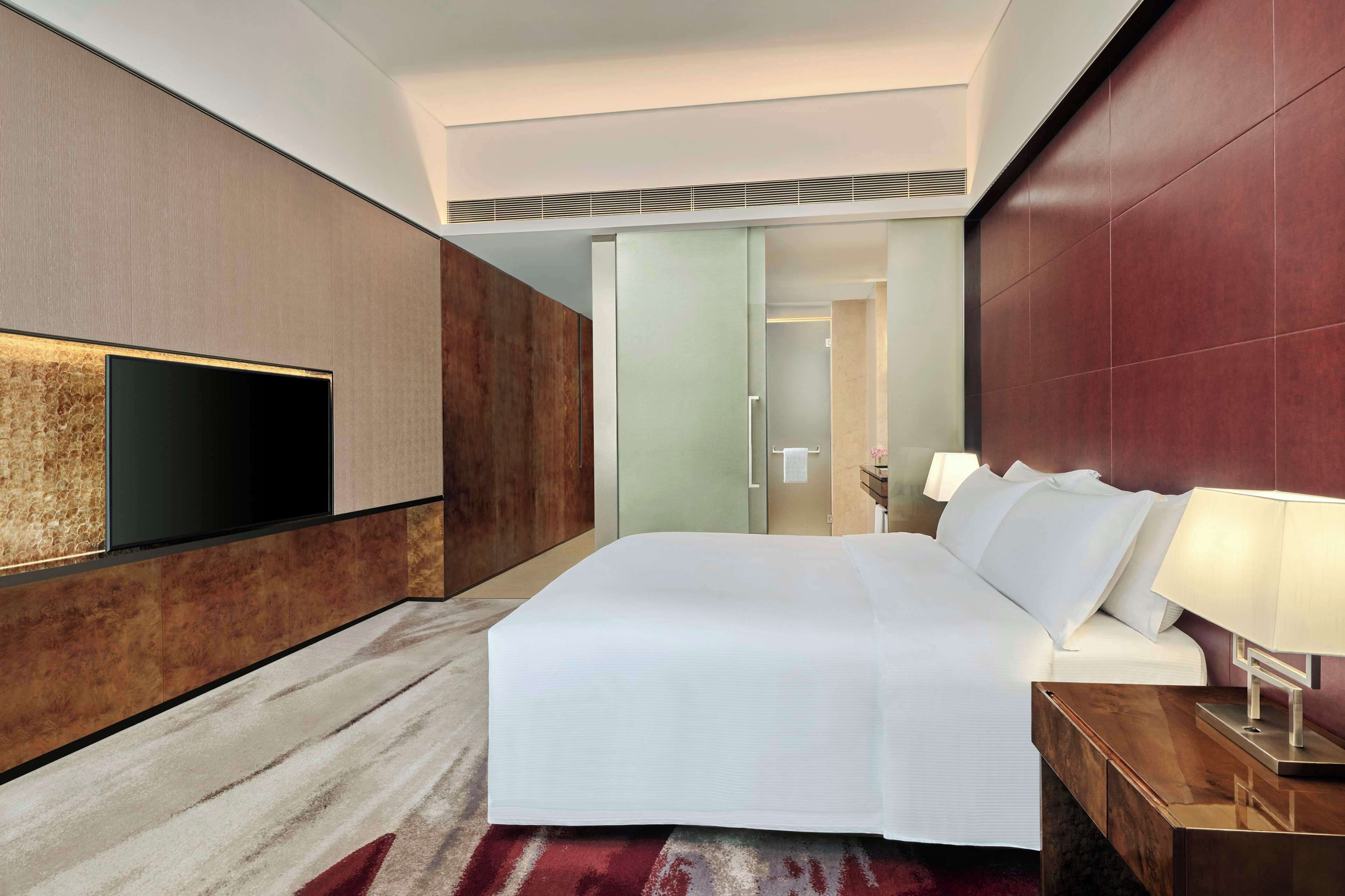 Una habitación de hotel moderna con una cama grande, un televisor de pantalla plana montado en la pared y un cabecero de madera.