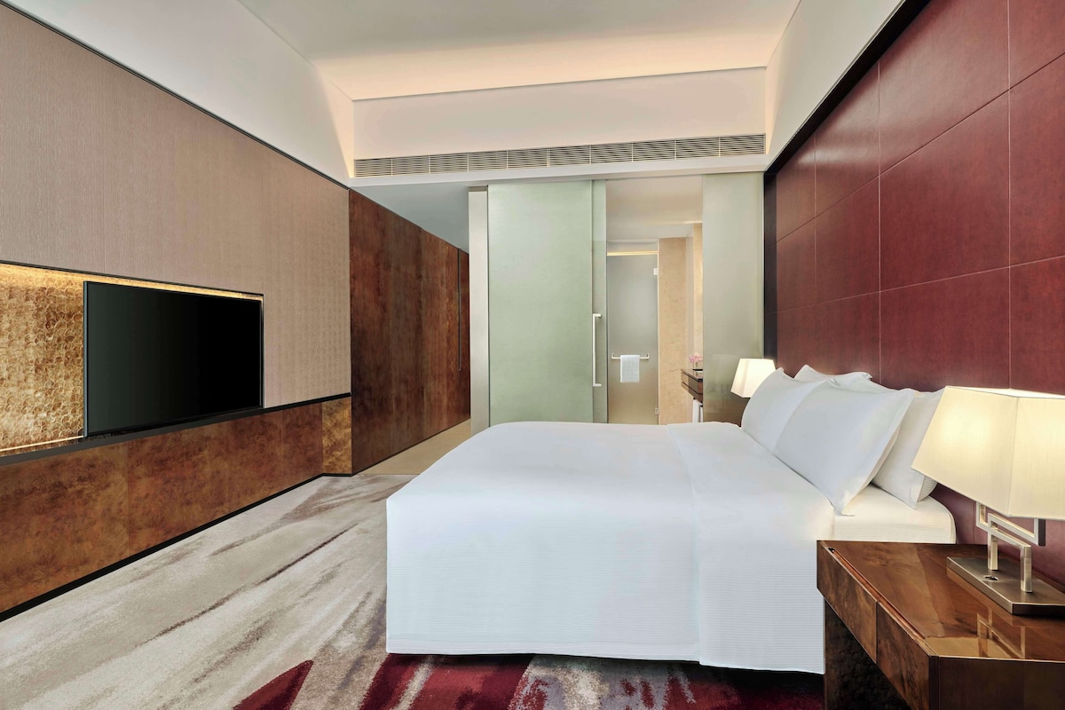 Una habitación de hotel moderna con una cama grande, un televisor de pantalla plana montado en la pared y un cabecero de madera.
