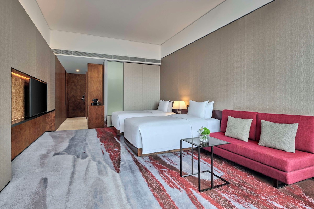 Una habitación de hotel con una cama grande, un sofá rojo, un televisor y una mesita.