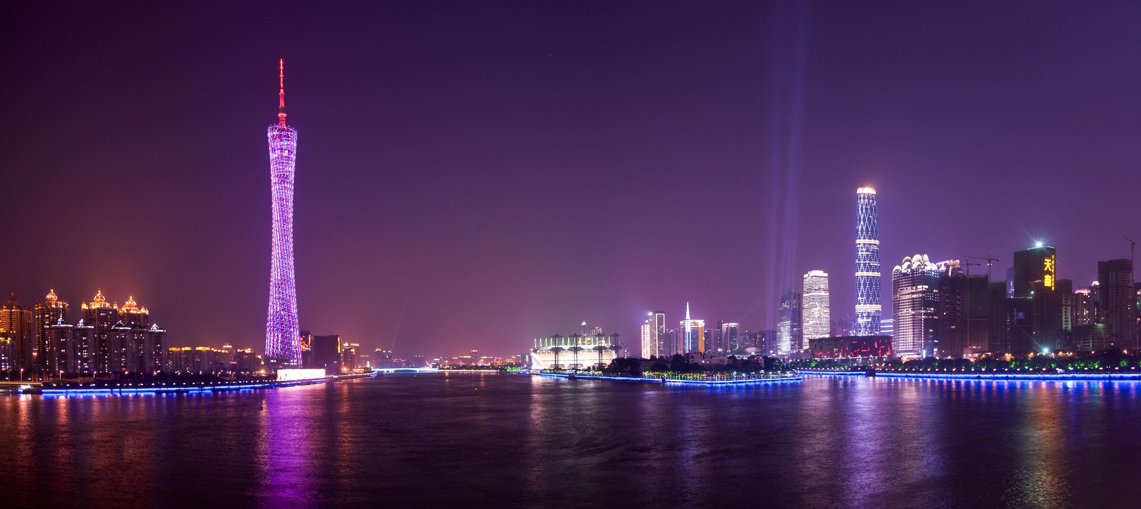 A nighttime cityscape with illuminated skyscrapers and a river reflecting the lights.