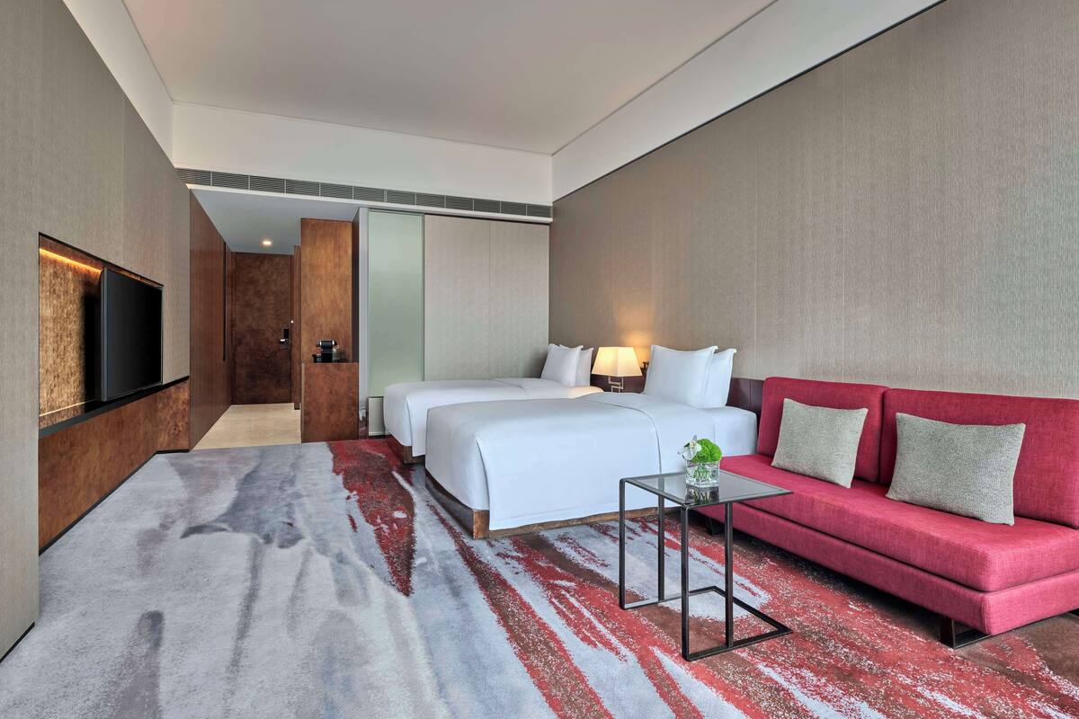 A hotel room with a large bed, a red sofa, a TV, and a small table.