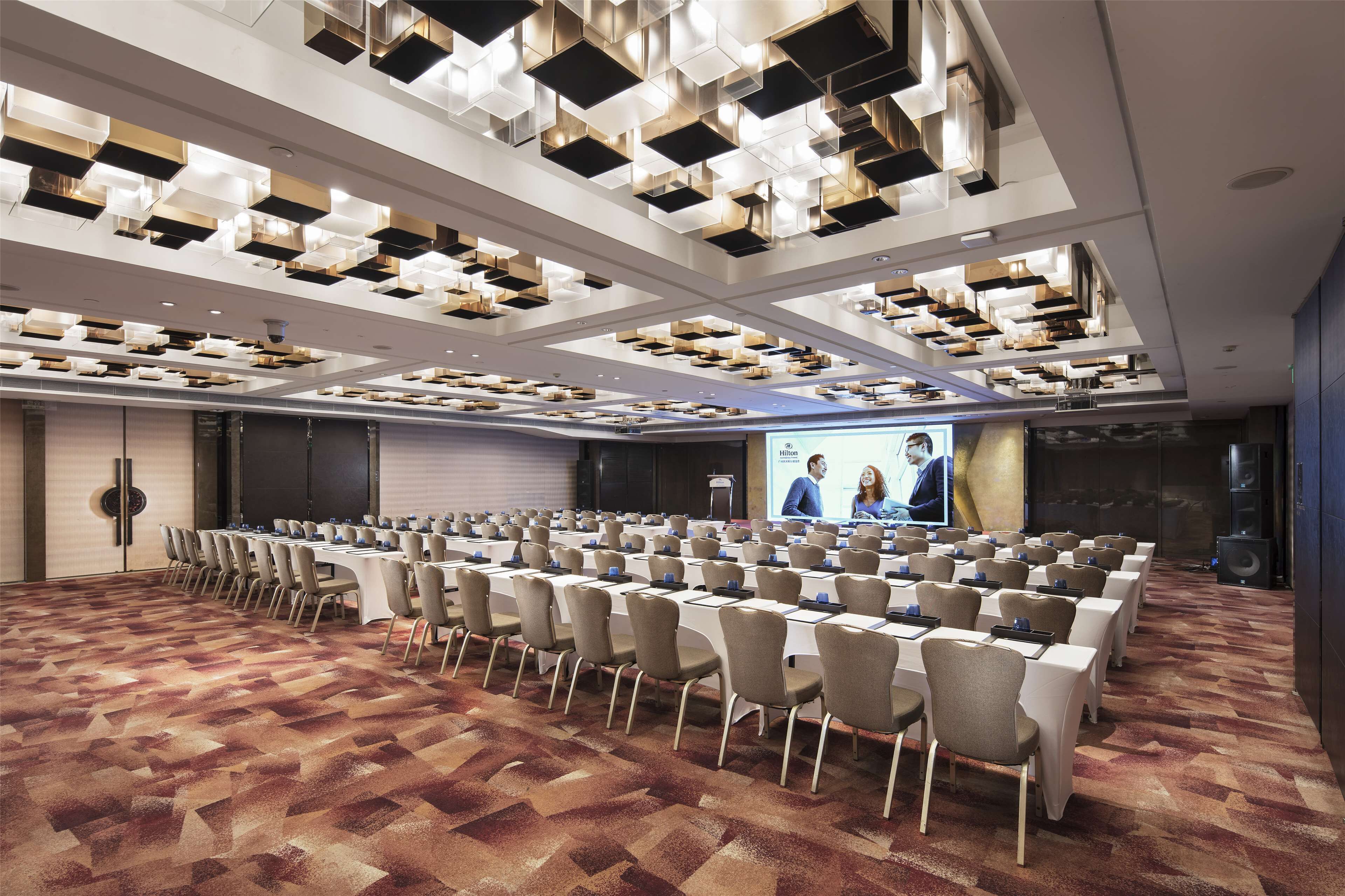 A conference room with a long table, rows of chairs, and a large screen for presentations.