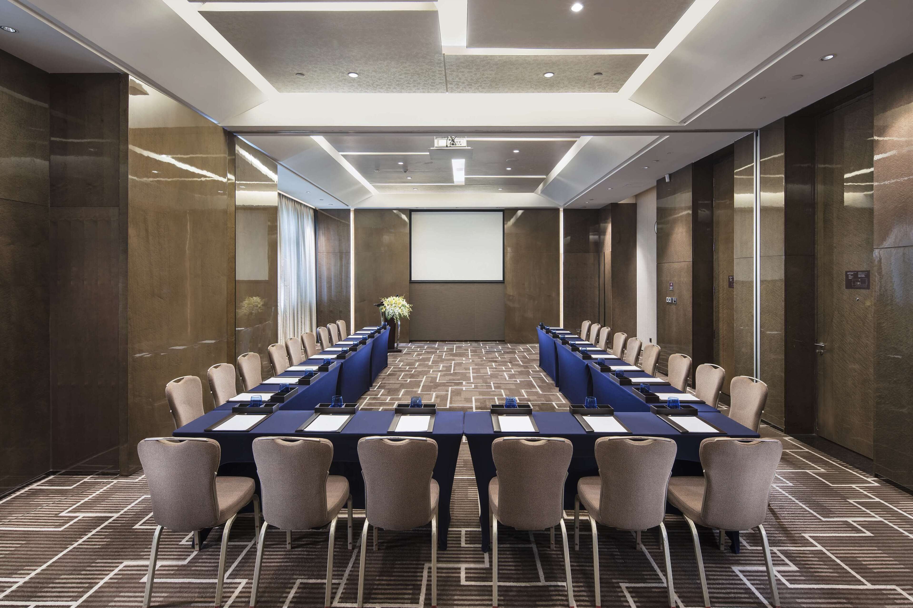 Una sala conferenze con un lungo tavolo, sedie, uno schermo per proiettore e un pavimento rivestito di moquette.