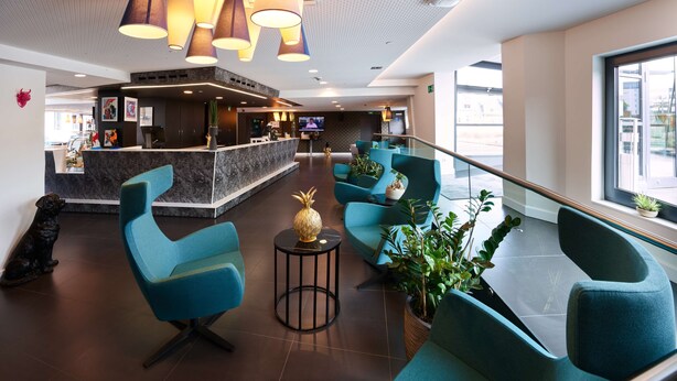 Un vestíbulo moderno con sillas color turquesa, un mostrador de recepción y un ventanal grande.