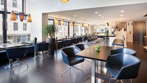Un restaurante moderno con techos altos, iluminación colgante y amplios ventanales que ofrecen vistas a la ciudad.