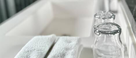 Un baño con un lavabo blanco, dos toallas enrolladas y dos botellas de vidrio transparente.
