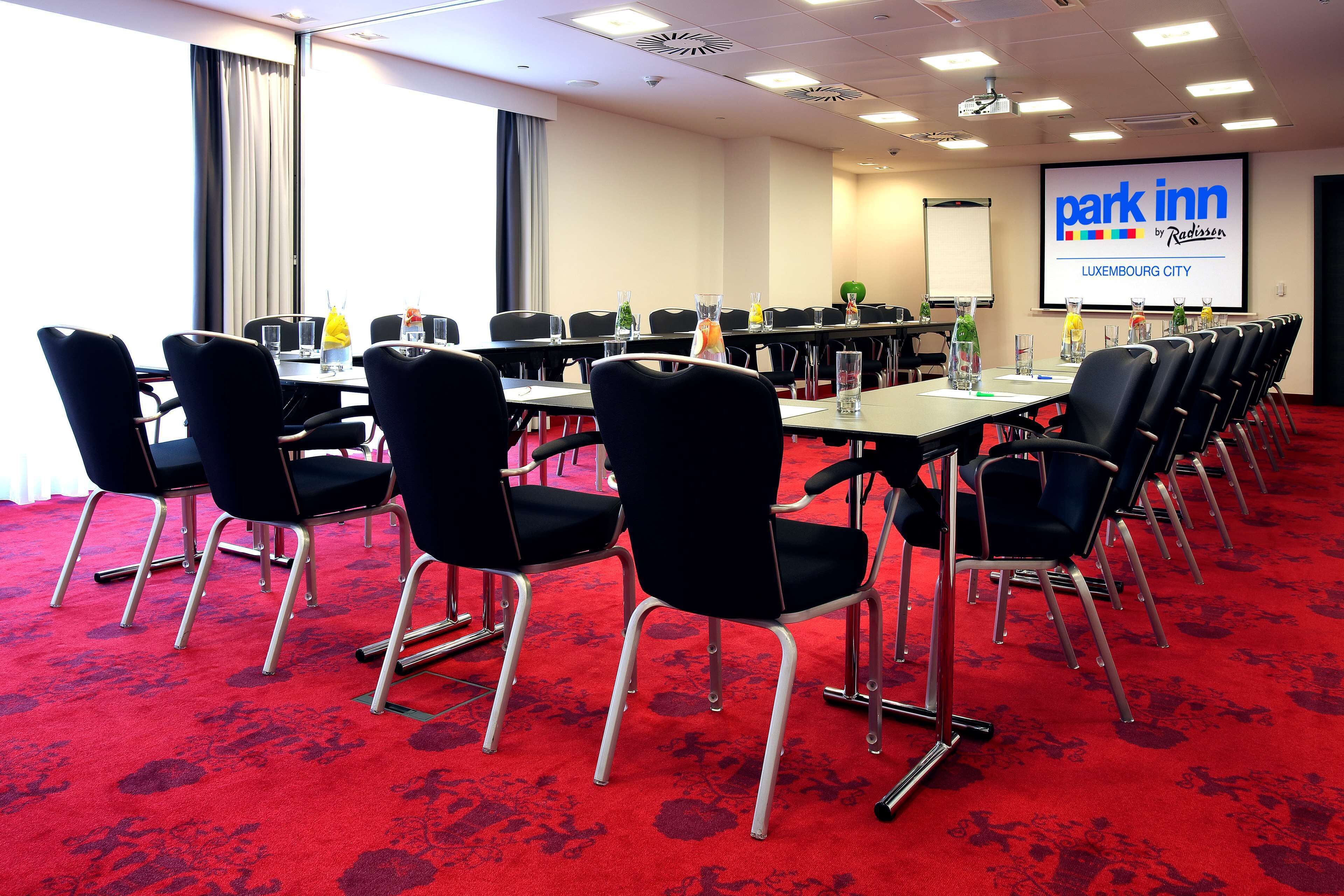 Une salle de conférence avec un tapis rouge, des chaises noires et un écran de présentation affichant le logo « Park Inn by Radisson ».
