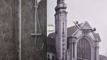 Une salle de bain moderne avec une douche à parois de verre, des murs en marbre et une affiche représentant un bâtiment historique.