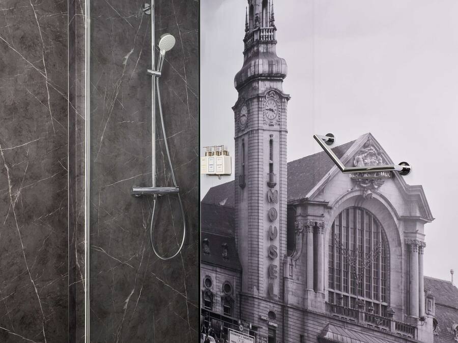 Une salle de bain moderne avec une douche à parois de verre, des murs en marbre et une affiche représentant un bâtiment historique.