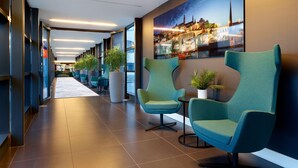Un moderno vestíbulo de hotel con sillas color turquesa, ventanas amplias y un mural con vista a la ciudad.