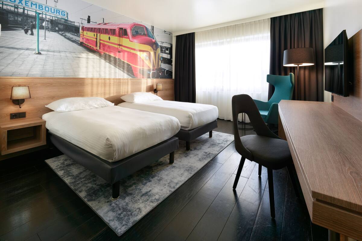 Habitación de hotel con dos camas, un escritorio, una silla, un televisor y un mural de un tren.