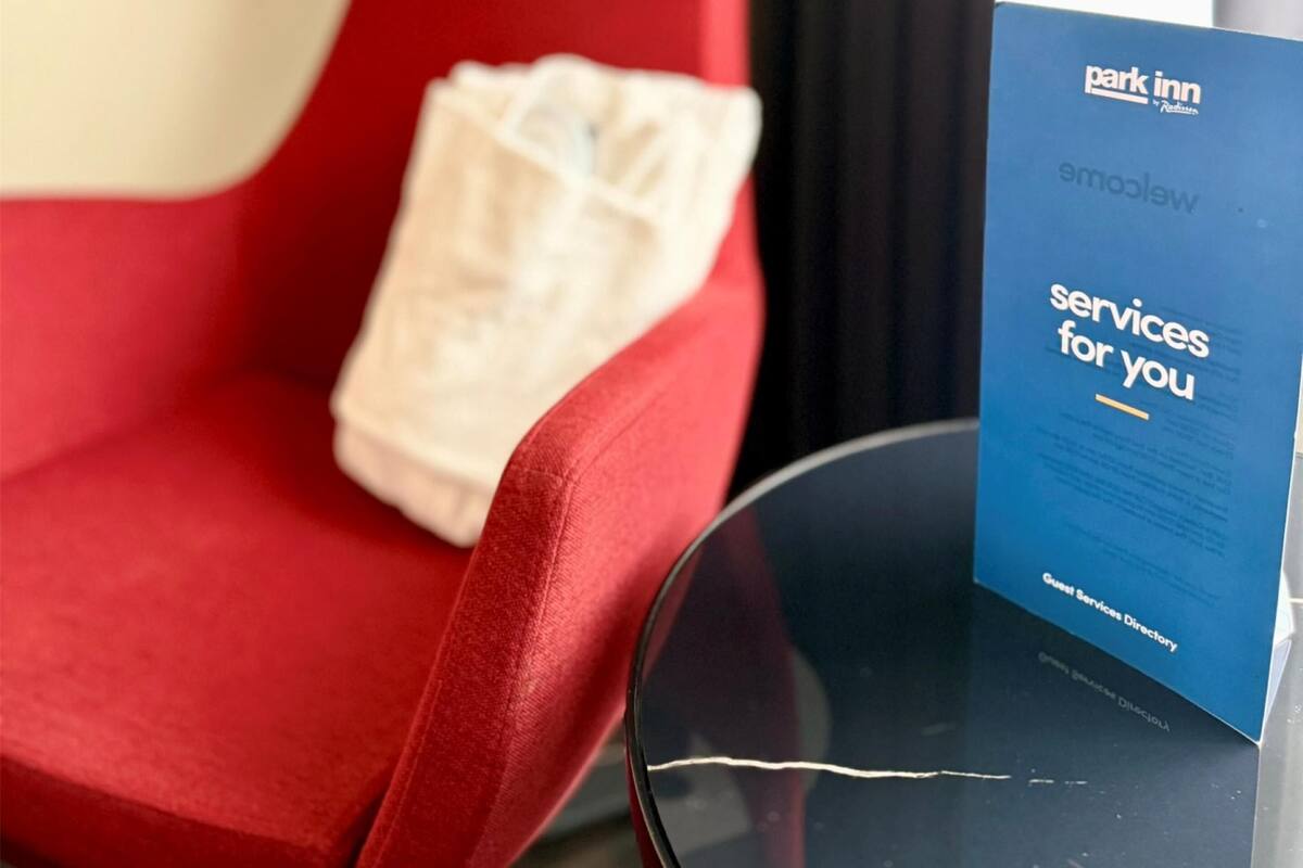 Una silla roja con un cojín blanco, una lámpara y un folleto azul titulado 'Park Inn Services for you' sobre una mesa.