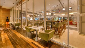 A modern restaurant with glass walls, wooden flooring, and green chairs. - Ibis Bengaluru Outer Ring Road (Bengaluru)