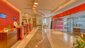 A modern hotel reception area with a red and white color scheme, a long reception desk, and a glass partition wall. - Ibis Bengaluru Outer Ring Road (Bengaluru)