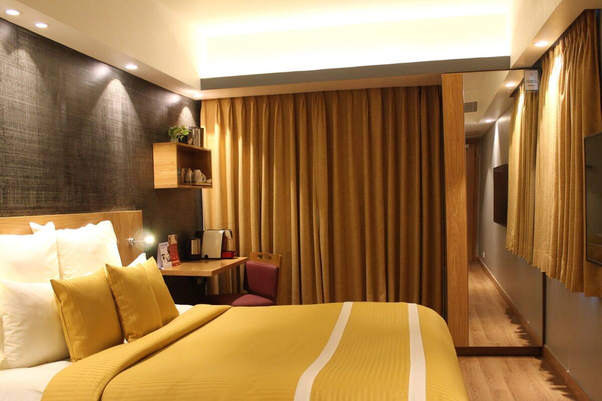 A hotel room with a large bed, a desk with a chair, a television, and a mirror.